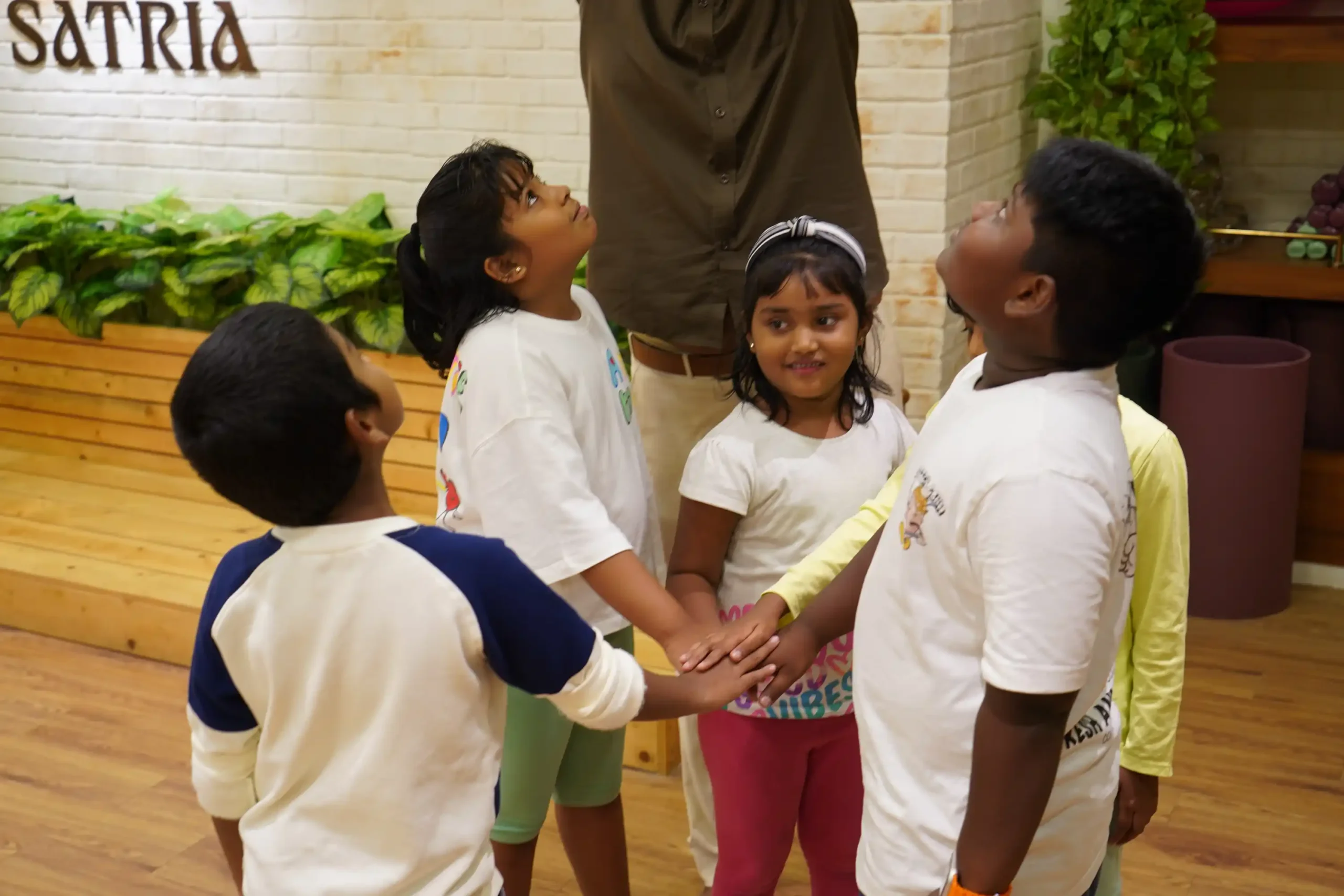 Children joining hands during a teamwork activity at Satria Studio